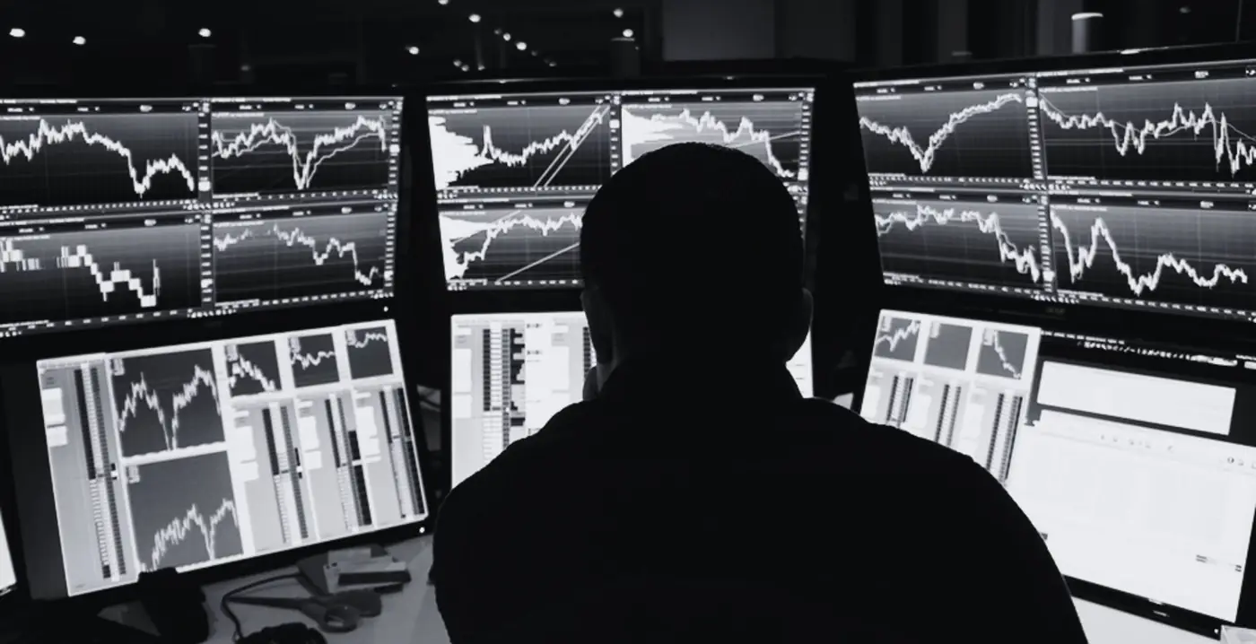 Un trader devant un mur d'écrans de cotation, en salle de marchés